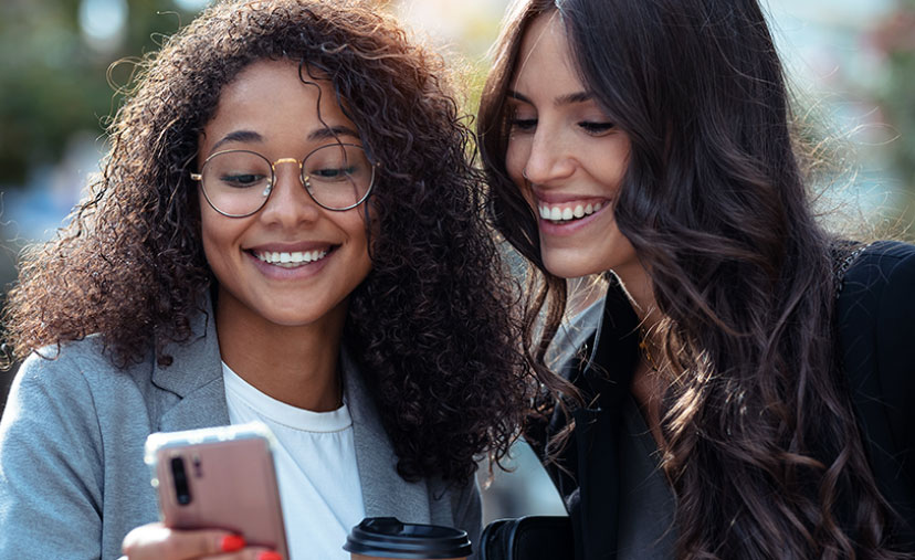 two smiling girlfriends looking at a mobile phone