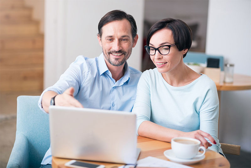 a dark-haired couple at a laptop in their living room