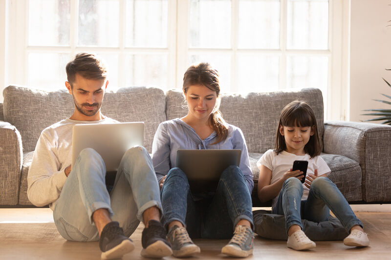 mother, father, and daughter sitting on the floor with laptops and phones
