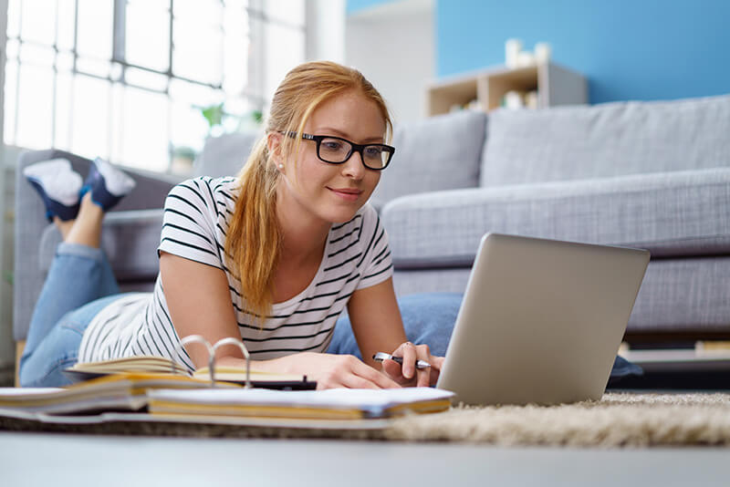 blonde girl with glasses lying on floor with laptop