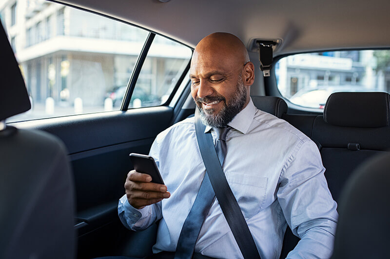 man looking at cell phone in back seat of car