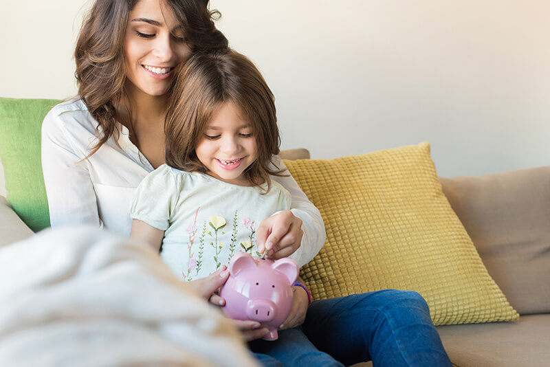 mother and daughter on couch with piggy bank